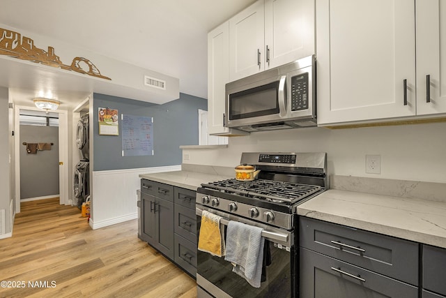 kitchen featuring stacked washer and dryer, white cabinetry, stainless steel appliances, light stone counters, and light wood-type flooring