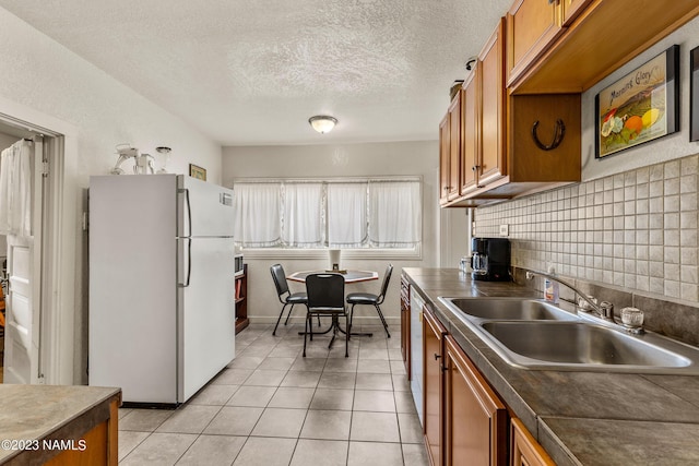 kitchen with white appliances, a textured ceiling, tasteful backsplash, light tile patterned floors, and sink