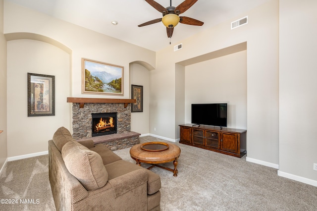 carpeted living room with a stone fireplace and ceiling fan