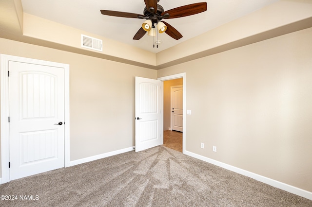 unfurnished bedroom with a raised ceiling, ceiling fan, and carpet