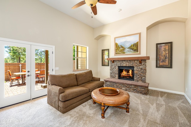 carpeted living room featuring french doors, ceiling fan, and a stone fireplace