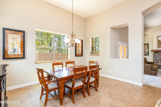 dining room featuring light tile patterned floors, a stone fireplace, high vaulted ceiling, and a chandelier