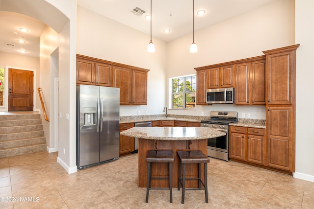 kitchen featuring appliances with stainless steel finishes, decorative light fixtures, a kitchen bar, a high ceiling, and a center island