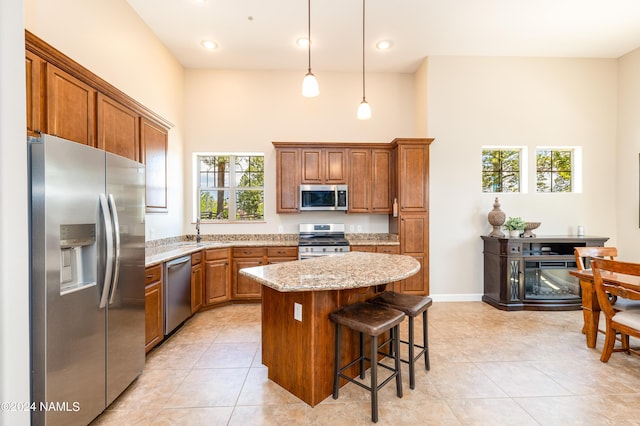 kitchen featuring light tile patterned floors, appliances with stainless steel finishes, hanging light fixtures, a center island, and light stone countertops