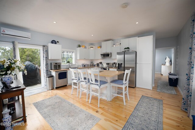 kitchen with light wood finished floors, a wall unit AC, stainless steel appliances, white cabinets, and recessed lighting
