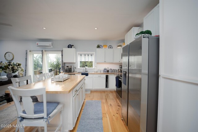 kitchen featuring a wall mounted air conditioner, white cabinets, wooden counters, stainless steel appliances, and a kitchen breakfast bar