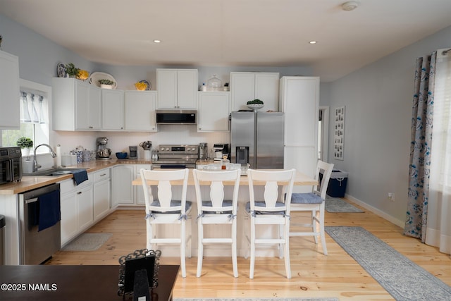 kitchen featuring ventilation hood, a sink, a center island, light wood-style flooring, and stainless steel appliances