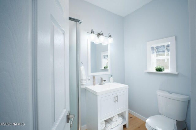 bathroom with toilet, vanity, wood finished floors, a shower with shower door, and baseboards