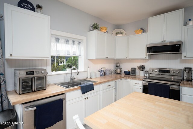 kitchen featuring white cabinets, a sink, stainless steel appliances, and butcher block counters