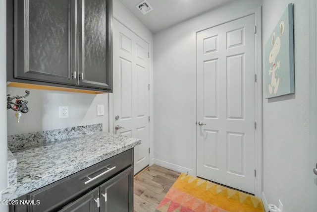 kitchen featuring light stone counters, light wood-style floors, visible vents, and baseboards