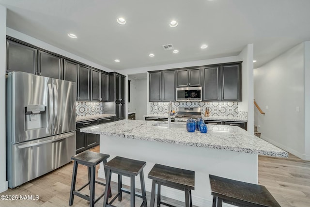 kitchen featuring light stone counters, stainless steel appliances, light wood-type flooring, and visible vents