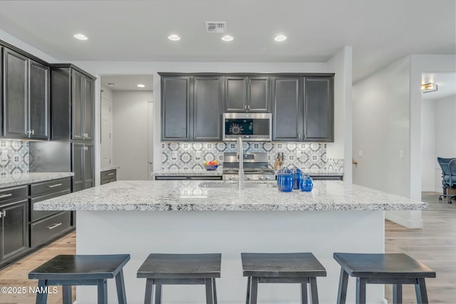 kitchen featuring stainless steel microwave, a breakfast bar, visible vents, and a sink