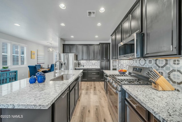 kitchen with visible vents, a sink, light stone countertops, stainless steel appliances, and a kitchen island with sink