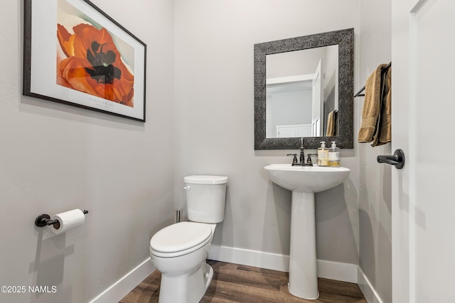 half bathroom with wood finished floors, toilet, and baseboards