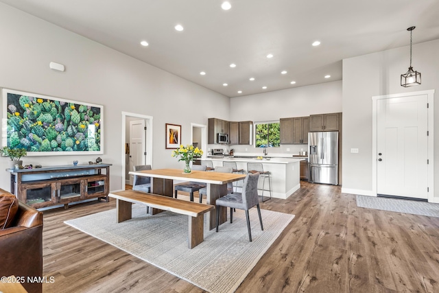 dining room featuring baseboards, a high ceiling, recessed lighting, and light wood-style floors