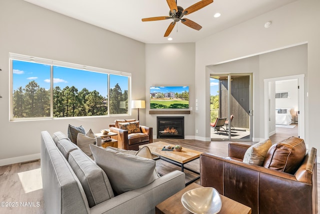 living area with recessed lighting, a ceiling fan, a glass covered fireplace, wood finished floors, and baseboards