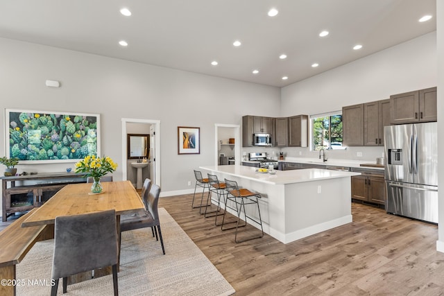 kitchen featuring stainless steel appliances, a high ceiling, a kitchen island, light countertops, and light wood-type flooring