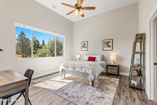 bedroom featuring a ceiling fan, visible vents, baseboards, and wood finished floors