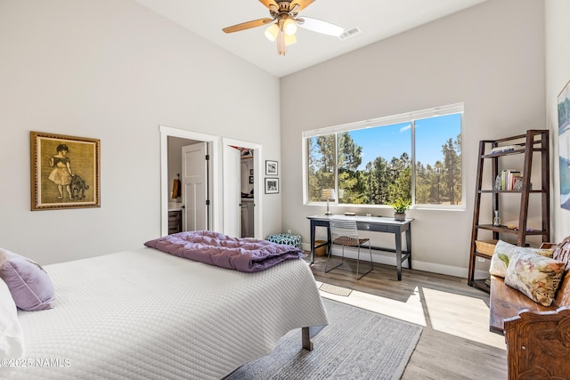 bedroom with baseboards, visible vents, wood finished floors, a walk in closet, and high vaulted ceiling