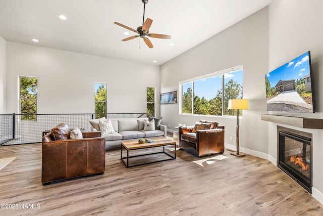 living room with baseboards, a glass covered fireplace, a towering ceiling, wood finished floors, and recessed lighting