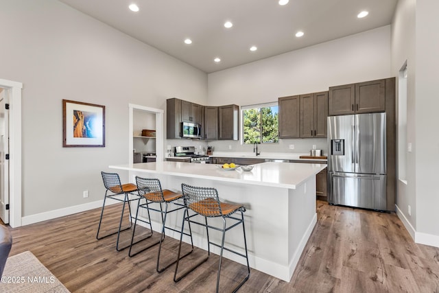 kitchen with a breakfast bar area, stainless steel appliances, light countertops, light wood-style flooring, and a high ceiling