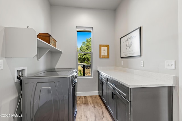 clothes washing area featuring light wood finished floors, separate washer and dryer, cabinet space, and baseboards