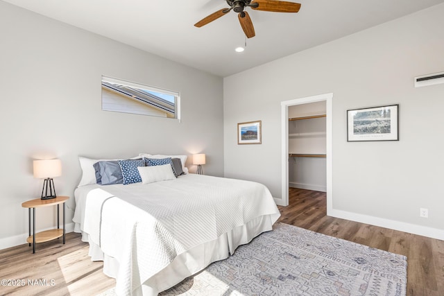 bedroom featuring wood finished floors, a ceiling fan, baseboards, a closet, and a walk in closet