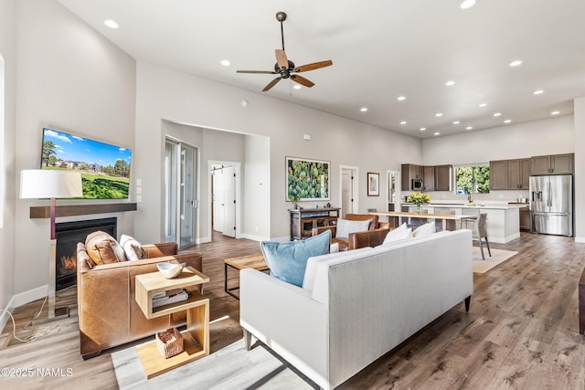 living area featuring recessed lighting, light wood-style flooring, a high ceiling, a glass covered fireplace, and baseboards