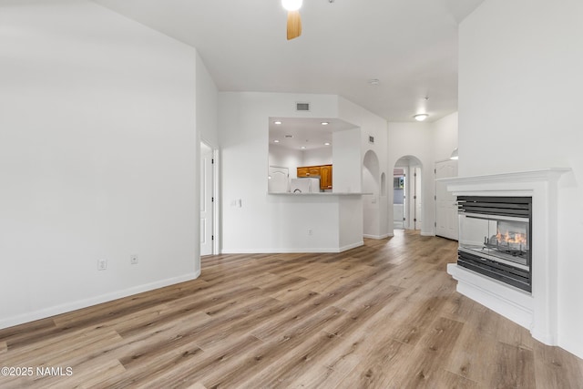 1401 N 4th St Unit 228, Flagstaff, AZ 86004 - unfurnished living room featuring ceiling fan, arched walkways, light wood-type flooring, a multi sided fireplace, and baseboards