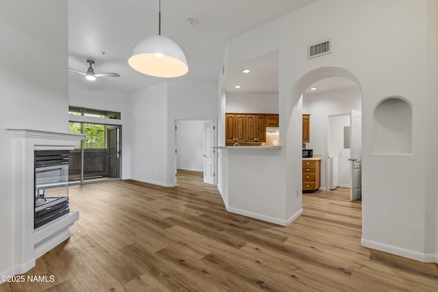 1401 N 4th St Unit 228, Flagstaff, AZ 86004 - unfurnished living room with light wood-style floors, baseboards, ceiling fan, a glass covered fireplace, and a towering ceiling