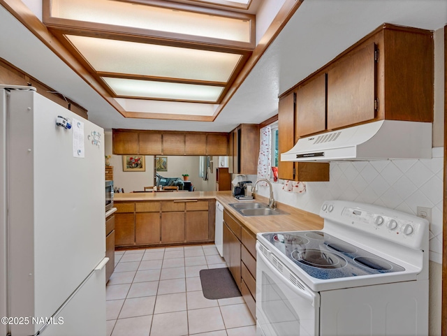 kitchen with white appliances, brown cabinetry, light countertops, under cabinet range hood, and a sink