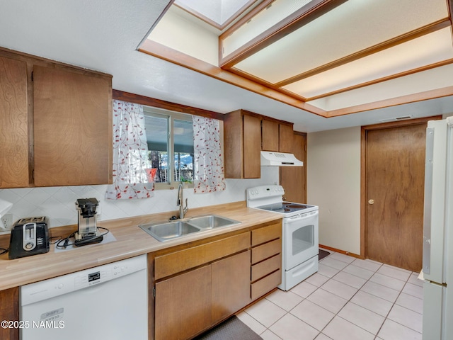 kitchen with white appliances, light countertops, under cabinet range hood, a sink, and light tile patterned flooring