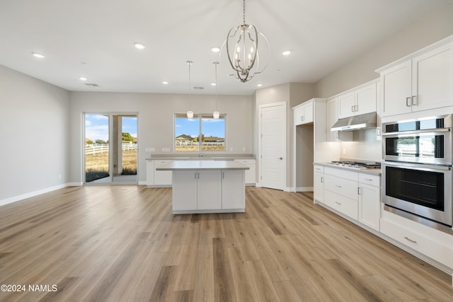 kitchen with hanging light fixtures, appliances with stainless steel finishes, white cabinets, light wood-type flooring, and a kitchen island