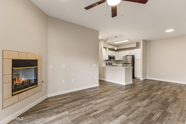 unfurnished living room with ceiling fan, wood-type flooring, and a tile fireplace