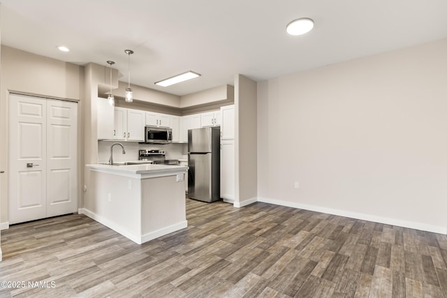 kitchen featuring appliances with stainless steel finishes, pendant lighting, white cabinets, kitchen peninsula, and light wood-type flooring