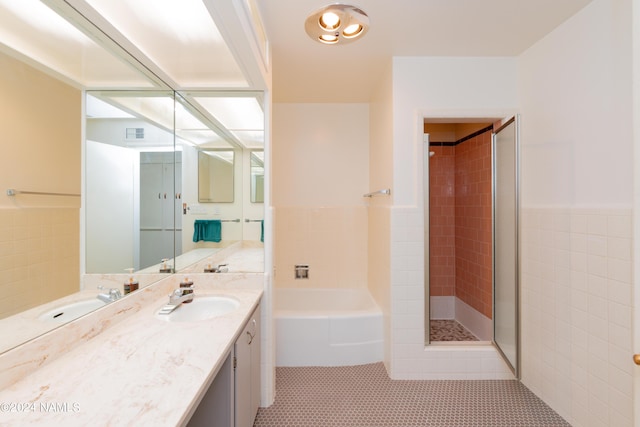 bathroom with plus walk in shower, tile patterned flooring, vanity, and tile walls