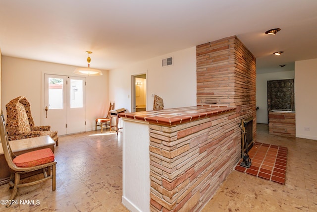 interior space featuring decorative light fixtures, a stone fireplace, and tile counters