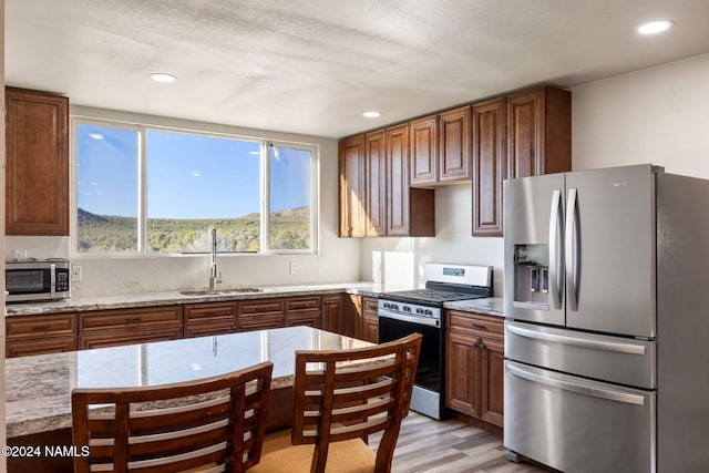 kitchen with light stone countertops, a textured ceiling, stainless steel appliances, sink, and light hardwood / wood-style flooring