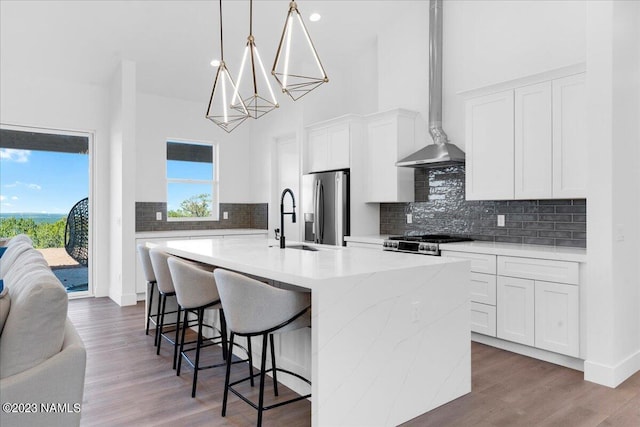 kitchen with white cabinetry, a kitchen island with sink, stove, pendant lighting, and stainless steel fridge