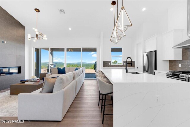 living room with a high ceiling, an inviting chandelier, sink, light hardwood / wood-style flooring, and a tiled fireplace