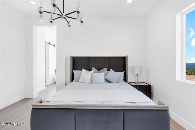 bedroom featuring an inviting chandelier, a barn door, and light wood-type flooring