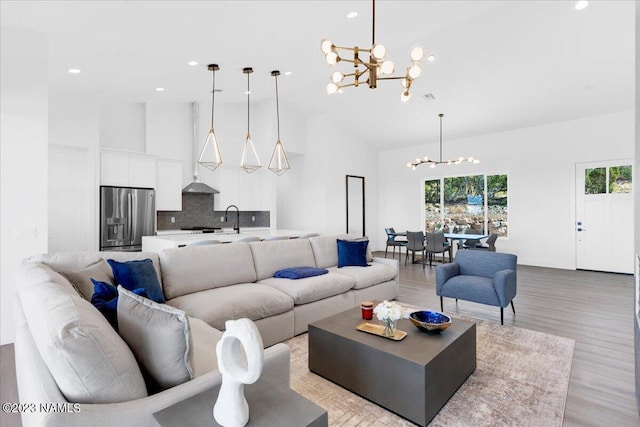 living room featuring high vaulted ceiling, sink, a notable chandelier, and light wood-type flooring