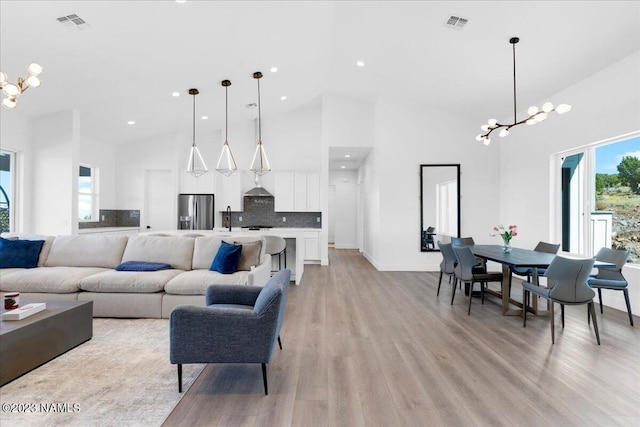 living room featuring light wood-type flooring, a chandelier, and high vaulted ceiling