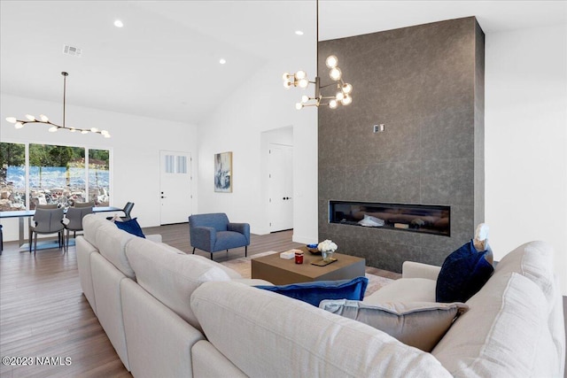 living room with high vaulted ceiling, wood-type flooring, a tile fireplace, and a chandelier