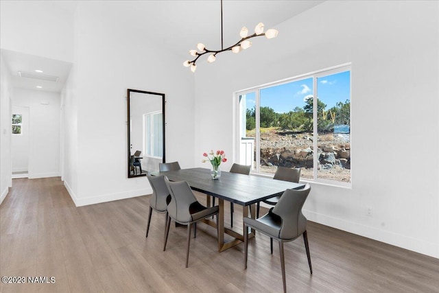 dining room with a towering ceiling, a healthy amount of sunlight, light wood-type flooring, and a notable chandelier