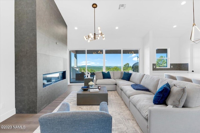 living room featuring light wood-type flooring, a notable chandelier, and a tiled fireplace