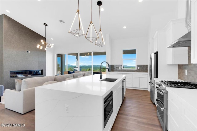 kitchen featuring hanging light fixtures, decorative backsplash, sink, stainless steel appliances, and a center island with sink