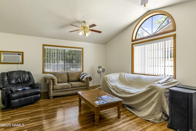 living area featuring vaulted ceiling, a wall mounted AC, wood finished floors, and a ceiling fan