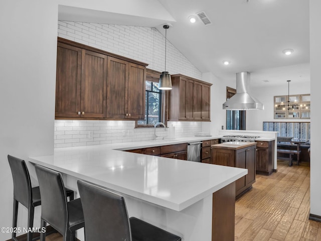 kitchen featuring kitchen peninsula, island range hood, a breakfast bar, and hanging light fixtures