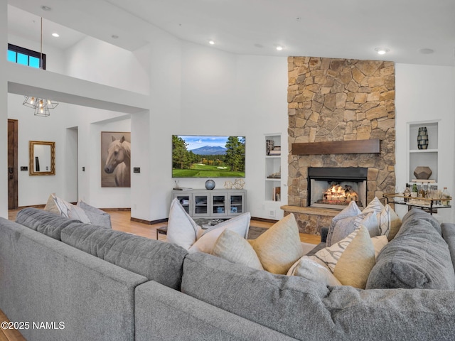 living room with built in features, light wood-type flooring, a towering ceiling, and a stone fireplace